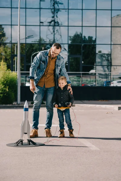 Feliz padre e hijo mirando el lanzamiento de cohetes modelo al aire libre - foto de stock