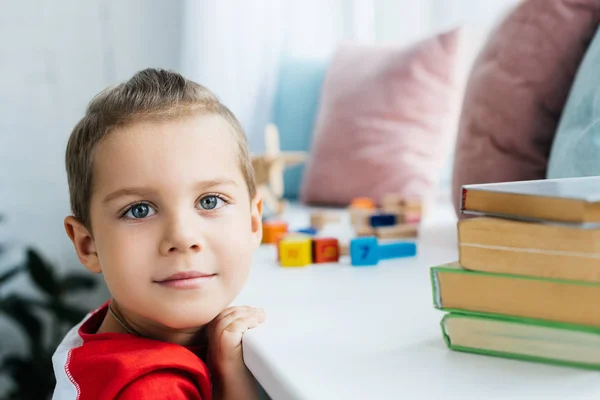 Niño de pie en la superficie con libros y bloques de colores en casa - foto de stock