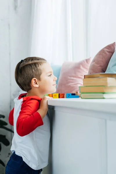Side view of child standing at surface with books and colorful blocks at home — Stock Photo