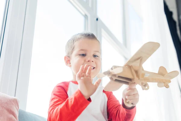 Sorrindo criança brincando com brinquedo avião de madeira em casa — Fotografia de Stock