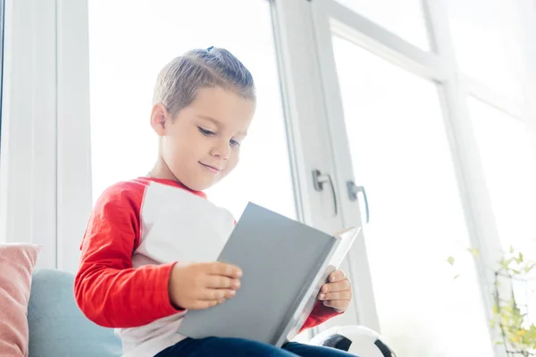 Criança sorrindo leitura livro na janela em casa — Fotografia de Stock