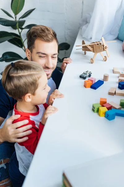 Pai abraçando filho enquanto de pé na superfície com brinquedos em casa — Fotografia de Stock