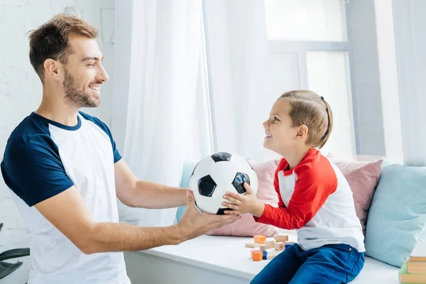 Alegre hombre e hijo con pelota de fútbol en casa - foto de stock