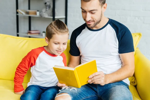 Retrato de padre leyendo libro para hijo pequeño en casa - foto de stock