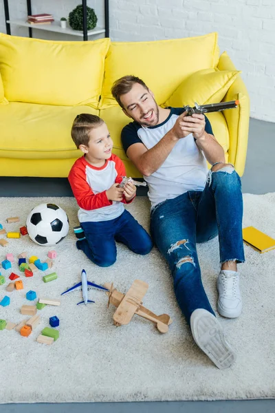 Улыбающийся мужчина и симпатичный сын играют с игрушками вместе на полу дома — стоковое фото
