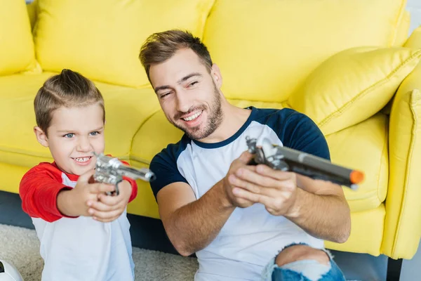 Retrato de alegre hijo y padre con pistolas de juguete en casa - foto de stock