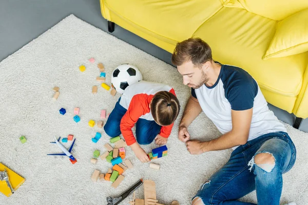 Vista aérea de padre e hijo pequeño jugando con bloques de madera juntos en el piso en casa - foto de stock