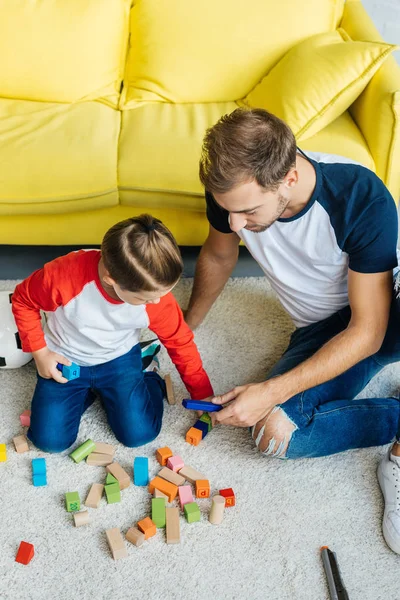 Pai e filho pequeno bonito brincando com blocos de madeira juntos no chão em casa — Fotografia de Stock