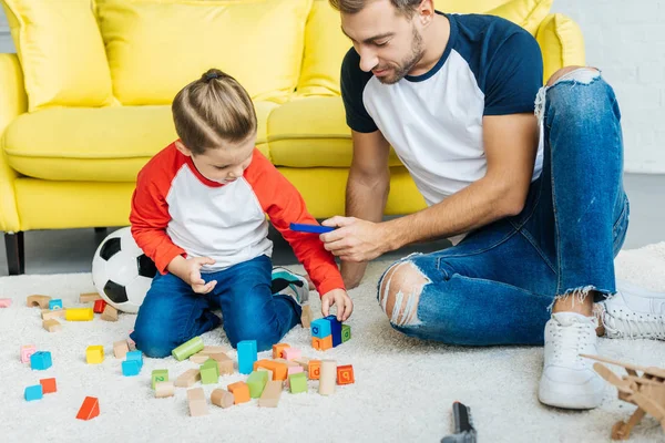 Padre y lindo hijo pequeño jugando con bloques de madera juntos en casa - foto de stock