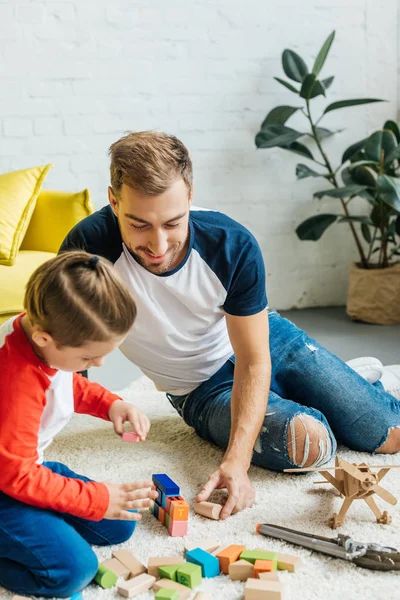 Padre y lindo hijo pequeño jugando con bloques de madera juntos en casa - foto de stock