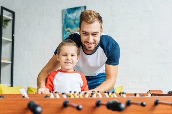 Sonrientes padre e hijo jugando futbolín juntos en casa - foto de stock