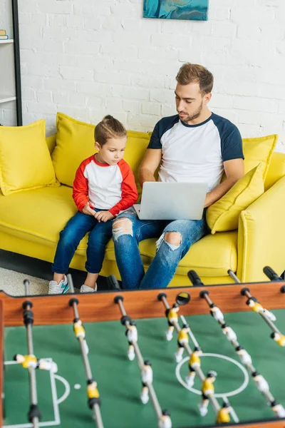Vater und Sohn nutzen gemeinsam Laptop, während sie sich zu Hause auf gelbem Sofa ausruhen — Stockfoto