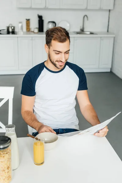 Sonriente hombre leyendo el periódico durante el desayuno en la cocina en casa - foto de stock