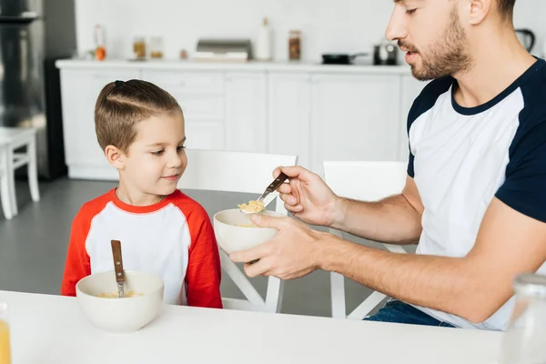 Father feeding son while having breakfast together in kitchen — Stock Photo