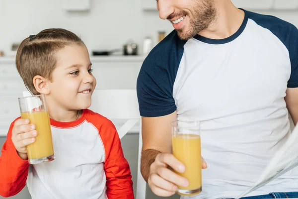 Teilansicht von Vater und glücklichem Sohn mit Gläsern Saft beim Frühstück in der heimischen Küche — Stockfoto