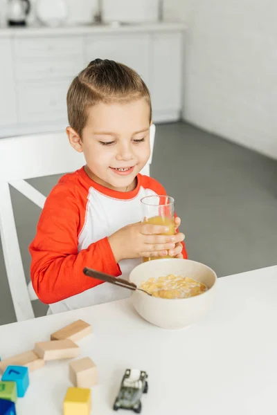 Портрет ребенка со стаканом сока, завтракающего на кухне дома — стоковое фото