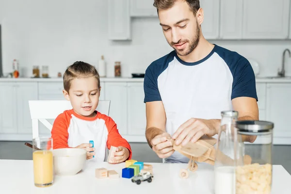 Pai e filho brincando com blocos de madeira e avião de brinquedo após o café da manhã na cozinha — Fotografia de Stock