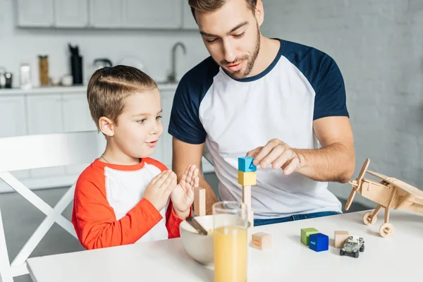 Padre e hijo jugando con bloques de madera después del desayuno en la cocina - foto de stock