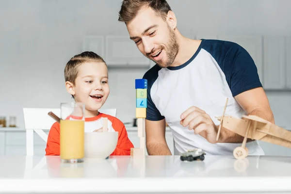 Bonito jovem pai e filho brincando com brinquedos na cozinha em casa — Fotografia de Stock