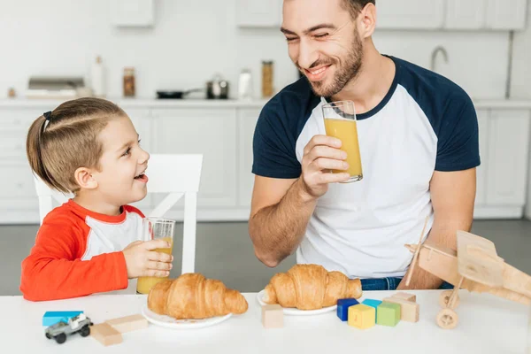 Bello giovane padre e figlio fare colazione con croissant e succo d'arancia insieme a casa — Foto stock