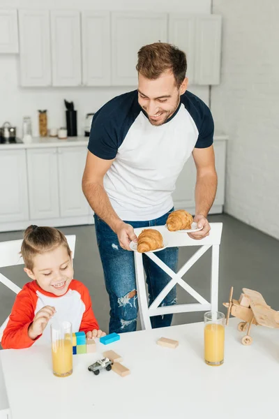 Hermoso joven padre e hijo teniendo croissants para el desayuno en casa - foto de stock