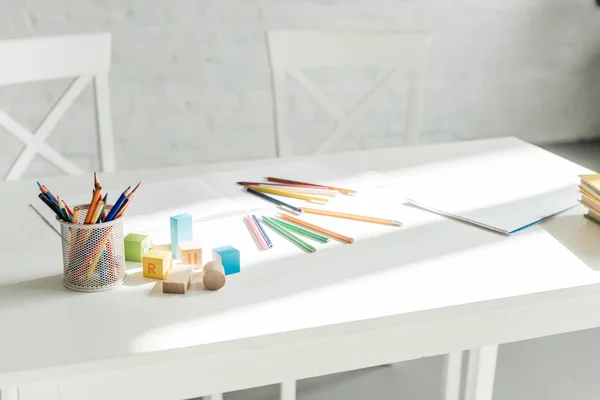 Plan rapproché de crayons de couleur avec album vierge et blocs de bois couchés sur la table — Photo de stock