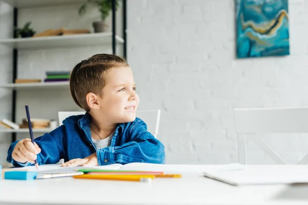 Cute little kid drawing with color pencils at home and looking away — Stock Photo