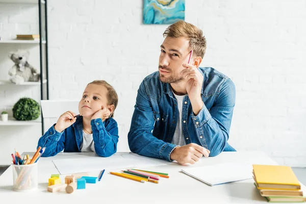 Nachdenklicher junger Vater zeichnet mit kleinem Sohn zu Hause — Stockfoto