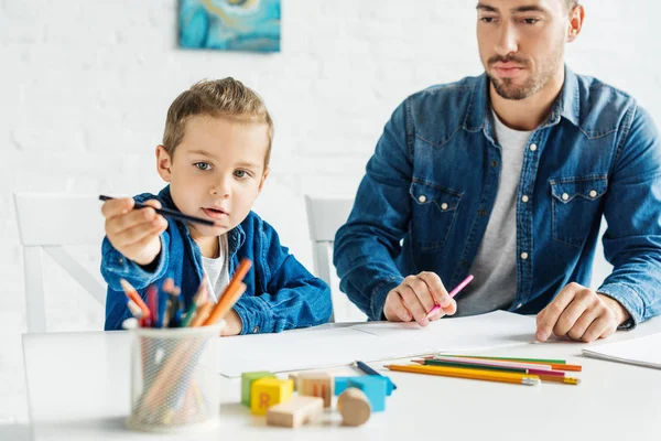 Красивий молодий батько малює з чарівним маленьким сином вдома — стокове фото