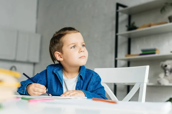 Thoughtful little kid drawing with color pencils at home — Stock Photo