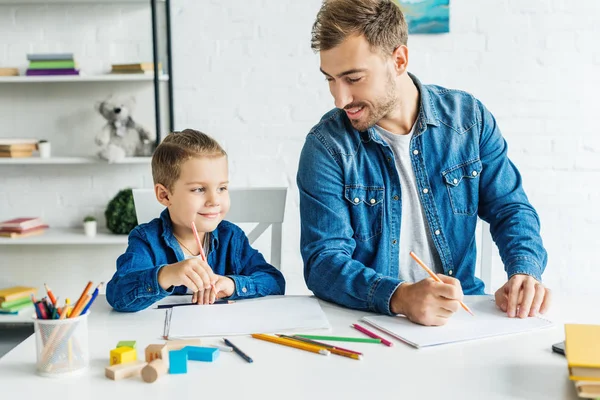 Feliz joven padre dibujo con hijo en casa - foto de stock