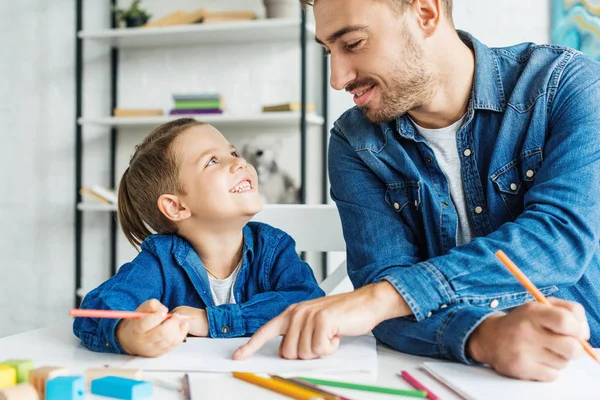 Sonriente joven padre dibujo con hijo en casa - foto de stock