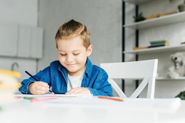 Niño sonriente dibujando con lápices de color en casa - foto de stock