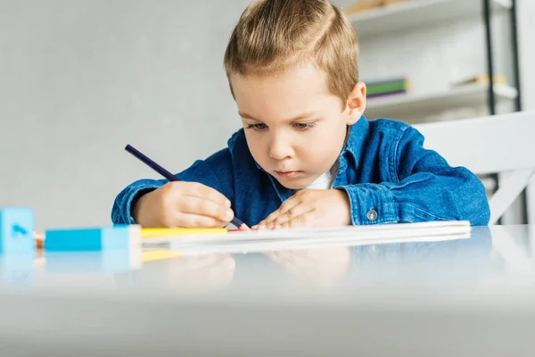 Pequeño niño concentrado dibujo con lápices de color en casa - foto de stock