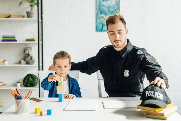 Guapo joven padre en uniforme de policía e hijo jugando juntos en casa - foto de stock