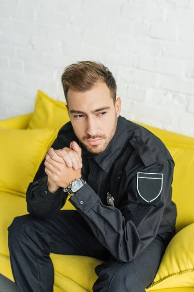 High angle view of thoughtful young policeman sitting on yellow couch in living room — Stock Photo