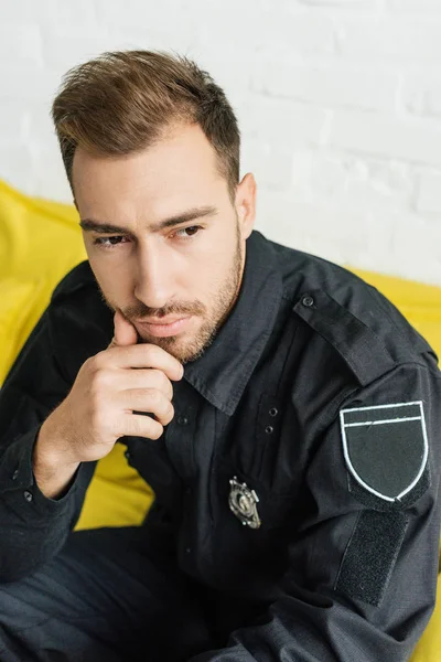 Close-up shot of thoughtful young policeman sitting on yellow couch — Stock Photo