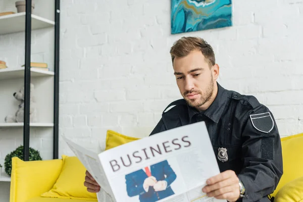 Attractive young policeman reading newspaper on couch — Stock Photo