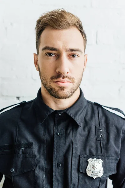 Close-up portrait of handsome young policeman in front of white brick wall — Stock Photo