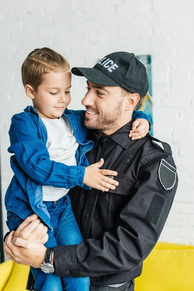 Schöner junger Vater in Polizeiuniform trägt seinen kleinen Sohn — Stockfoto