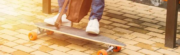 Wide cropped shot of man with leather backpack and skateboard sitting on bench on street — Stock Photo