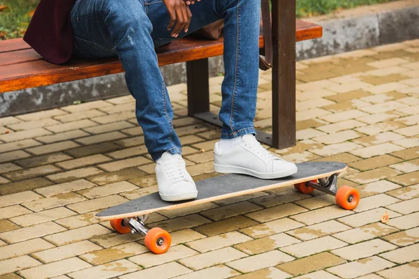 Tiro cortado de homem com skate sentado no banco — Fotografia de Stock