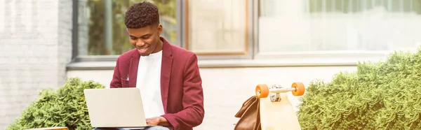 Wide toned shot of happy african american freelancer using laptop on street — Stock Photo