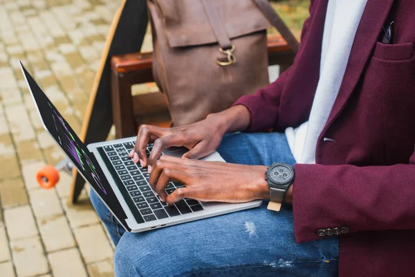 Cropped shot of freelancer using laptop on bench with leather backpack and skateboard — Stock Photo