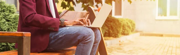 Cropped wide shot of freelancer using laptop on bench with skateboard — Stock Photo