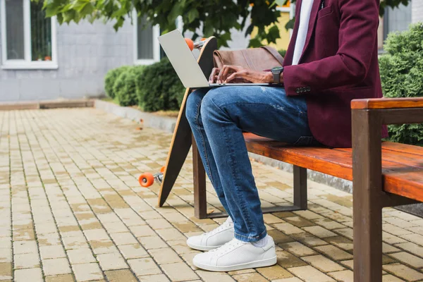 Cropped shot of freelancer using laptop on bench with skateboard — Stock Photo