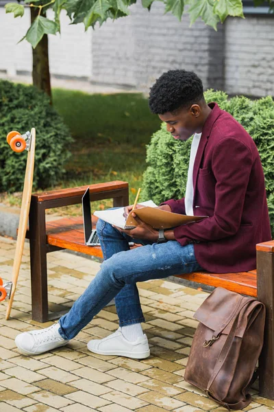 Junge afrikanisch-amerikanische Studentin schreibt in Notizbuch auf der Straße — Stockfoto