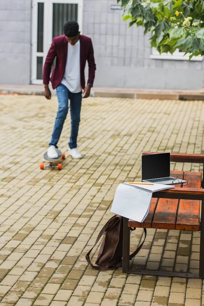 Молодий чоловік на вулиці з ноутбуком і блокнотом на лавці на передньому плані — стокове фото
