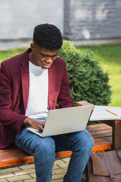 Afroamericano joven freelancer usando portátil en banco - foto de stock