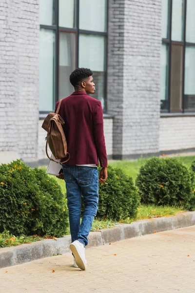 Rear view of young student with backpack and notebooks walking by street — Stock Photo